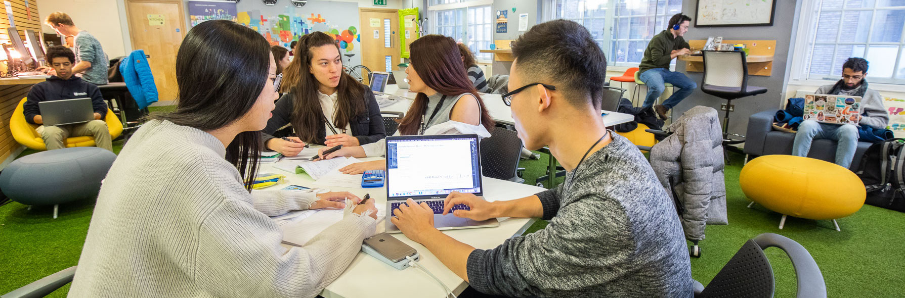 Young people in a coworking space. Some are working on computers and some are talking to each other.